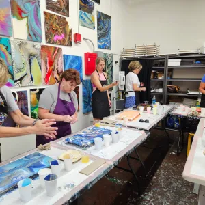 People painting abstract art in a busy studio with colorful artworks on the walls.