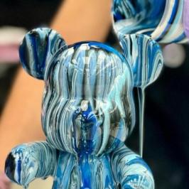 Paint poured over a bear-shaped figurine creating a striped blue pattern.
