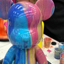 Colorful bear-shaped figurine with paint dripped over it.