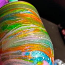 Colorful swirling patterns on a tumbler with green, orange, and blue hues.