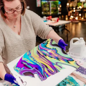 Person creating colorful abstract art on canvas with gloves in studio.