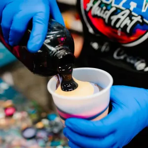 Person in blue gloves pouring black liquid into a colorful cup.