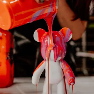 Person pouring colorful paint over a white bear-shaped figurine.